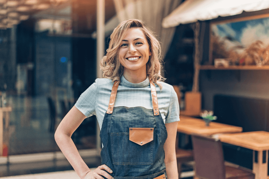 female business owner in an apron standing in front of a restaurant