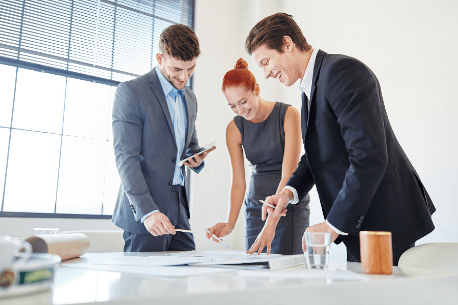 three business people standing around a table looking at a piece of paper