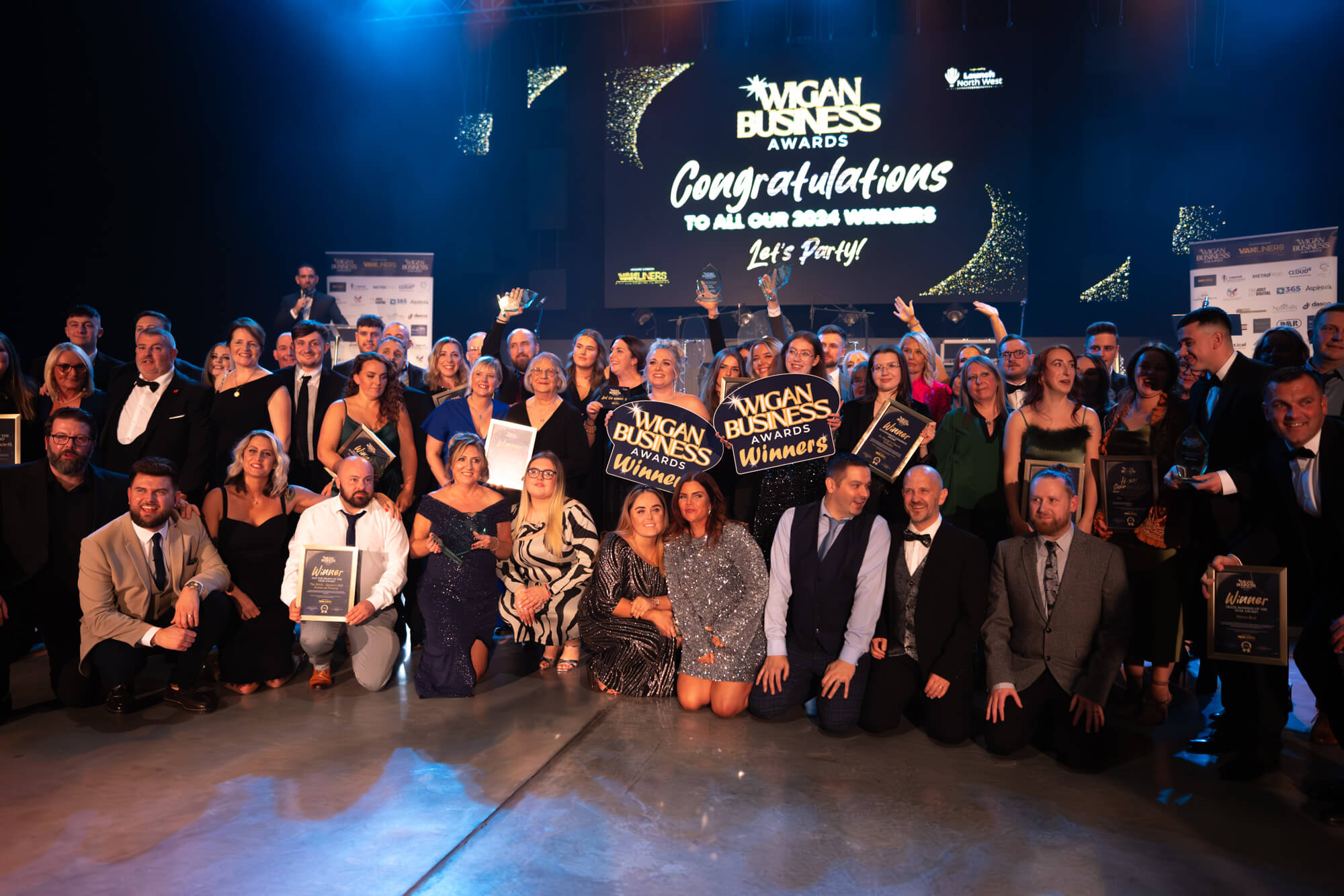 All the Wigan Business Awards 2024 winners in front of the stage holding their trophies and certificates