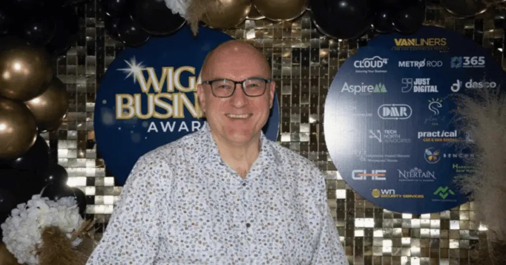 Wigan Business Awards Sponsor Phil Paramore from Plan-It-ESG Smiling in front of a gold back drop