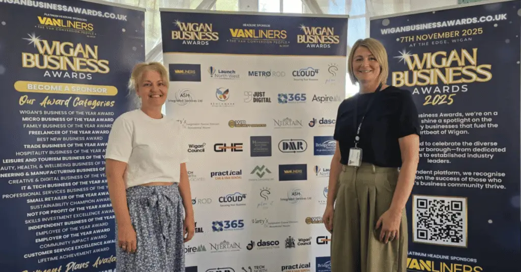 Image shows L-R Wigan Business Organiser & Creative Director Jo Leigh from Launch NW with Jo Yates Company Director at Metro Rod stood smiling in from of the Sponsor logo banners