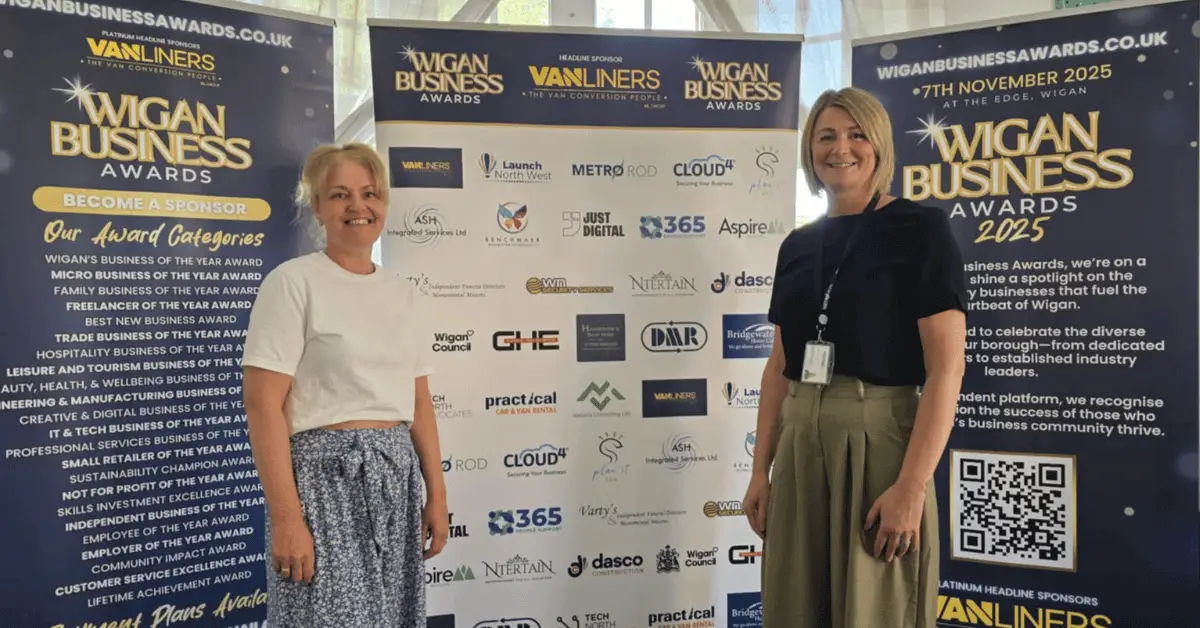 Image shows L-R Wigan Business Organiser & Creative Director Jo Leigh from Launch NW with Jo Yates Company Director at Metro Rod stood smiling in from of the Sponsor logo banners