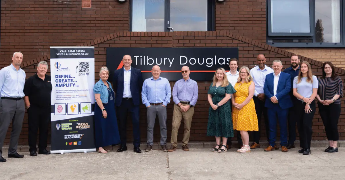 Team picture of the staff at Tibury Douglas stood smiling in front of their sign with Wigan Business Awards Organiser Nichola Howard