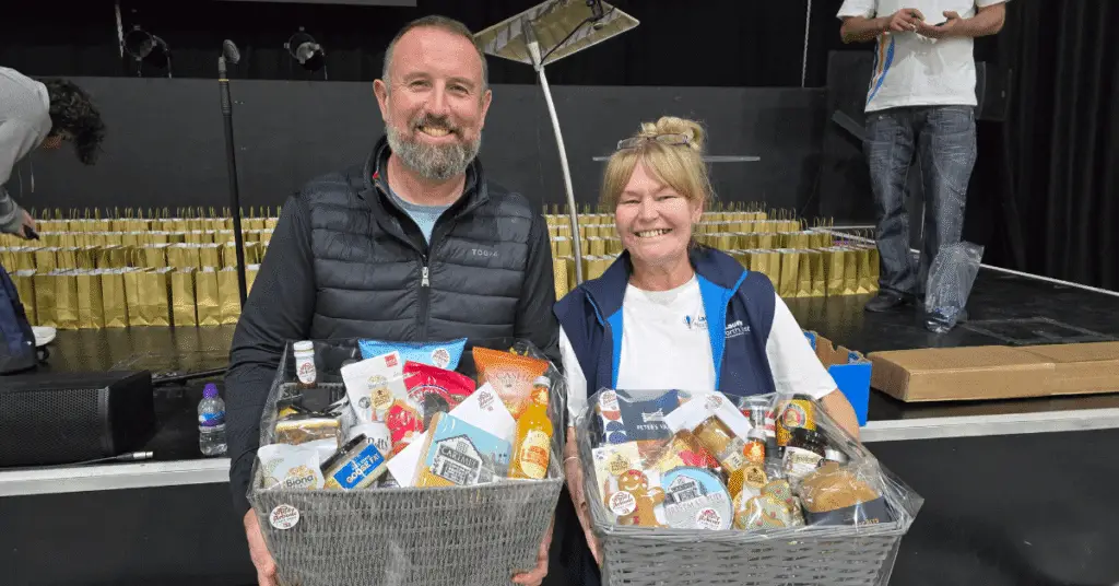 Geoff from Windy Arbour Farm shop with Nichola Howard from Wigan Business Awards smiling at the camera hold two food hampers