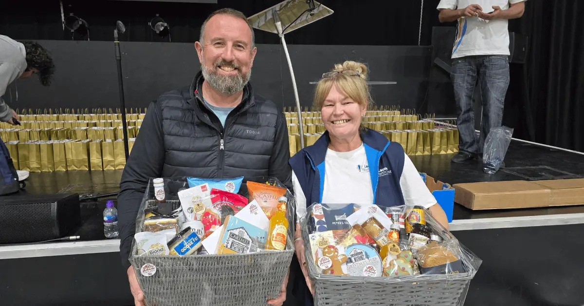 Geoff from Windy Arbour Farm shop with Nichola Howard from Wigan Business Awards smiling at the camera hold two food hampers