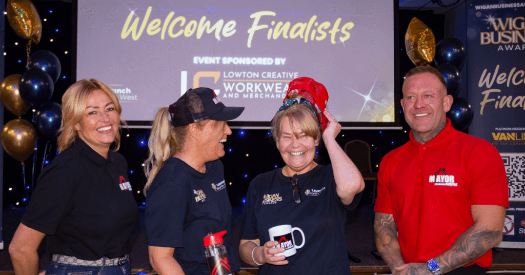 Four people laugh and pose at a Wigan Business Awards finalists event, in front of a “Welcome Finalists” screen and balloon display.