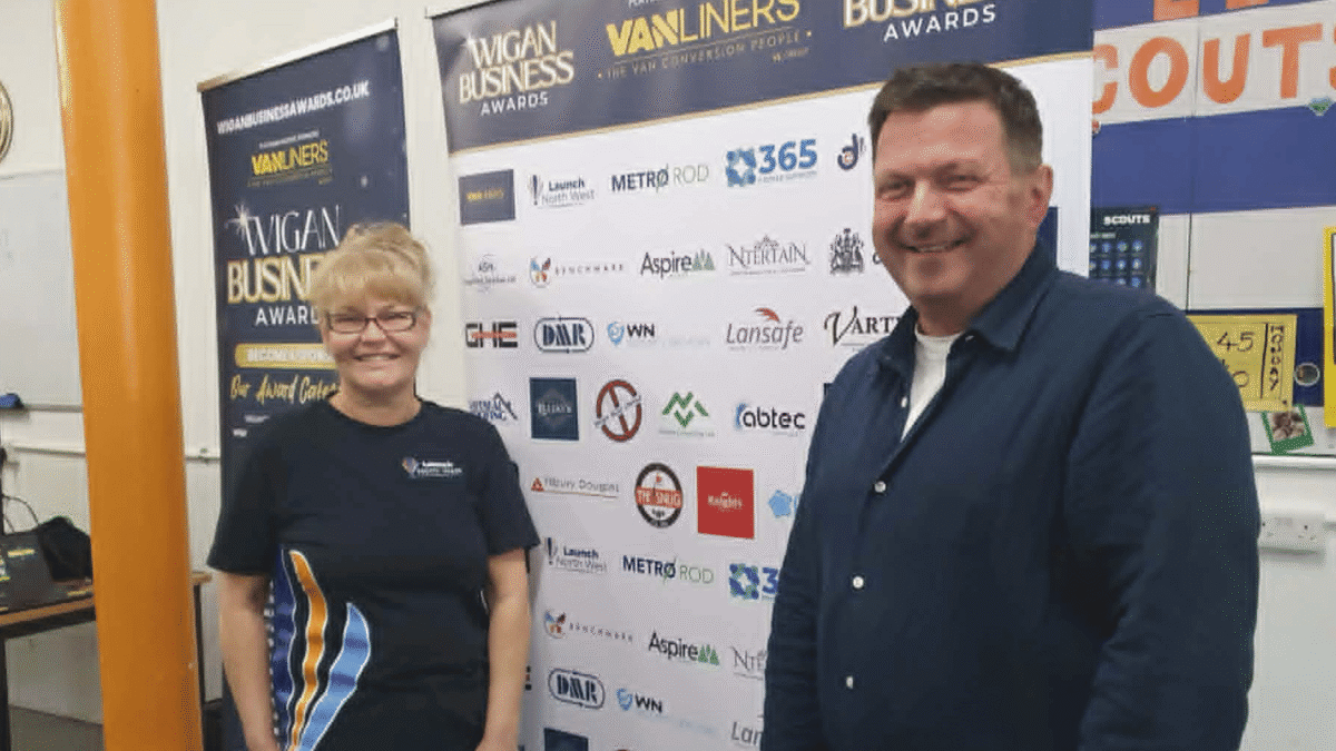 James Carman of 365 People Support and Wigan Business Awards organiser Nichola Howard standing in front of the Wigan Business Awards sponsor backdrop during the 2026 campaign.