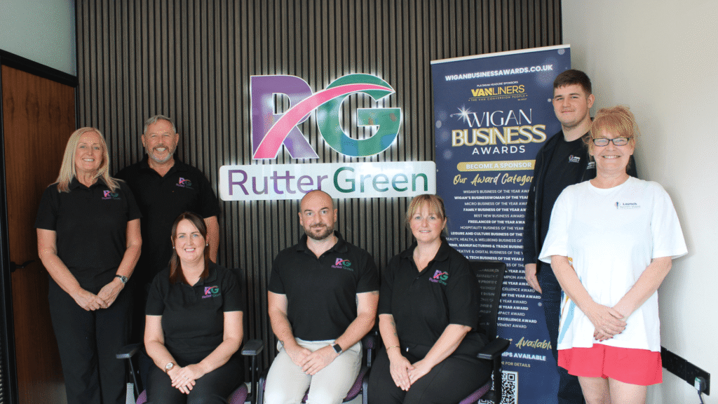 Rutter Green Estate Agents team members pose inside their office alongside a Wigan Business Awards banner.